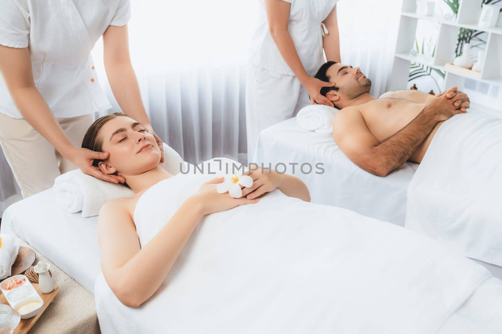 Caucasian couple enjoying relaxing anti-stress head massage and pampering facial beauty skin recreation leisure in dayspa modern light ambient at luxury resort or hotel spa salon. Quiescent