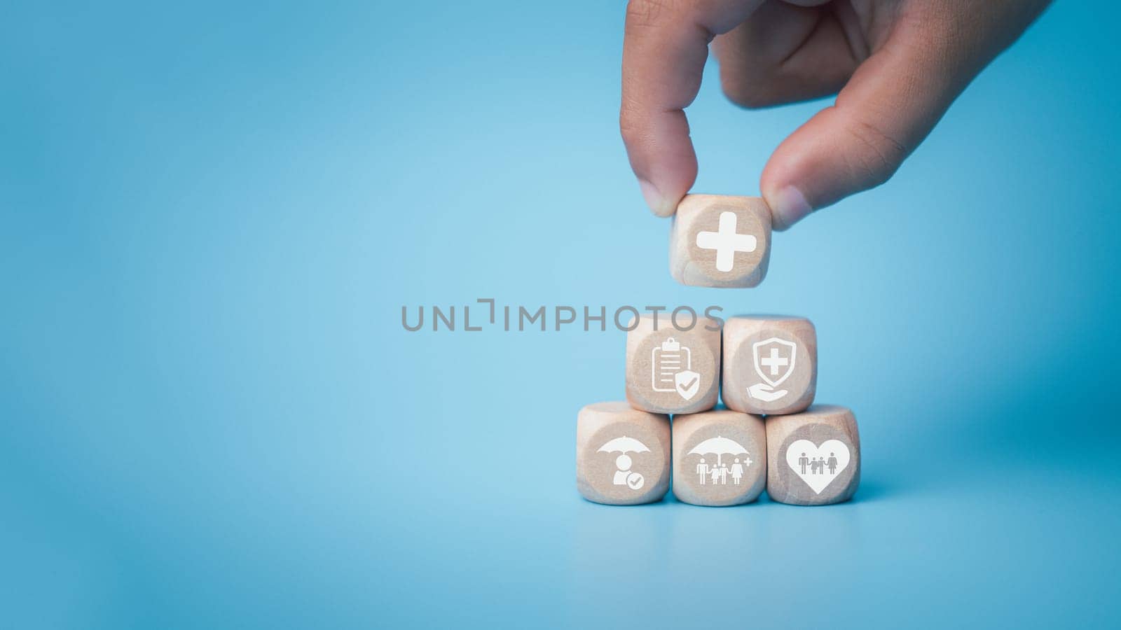 Health insurance and healthcare concept, human hand holds wooden block with icons about health insurance and healthcare access, retirement planning on blue background. by Unimages2527