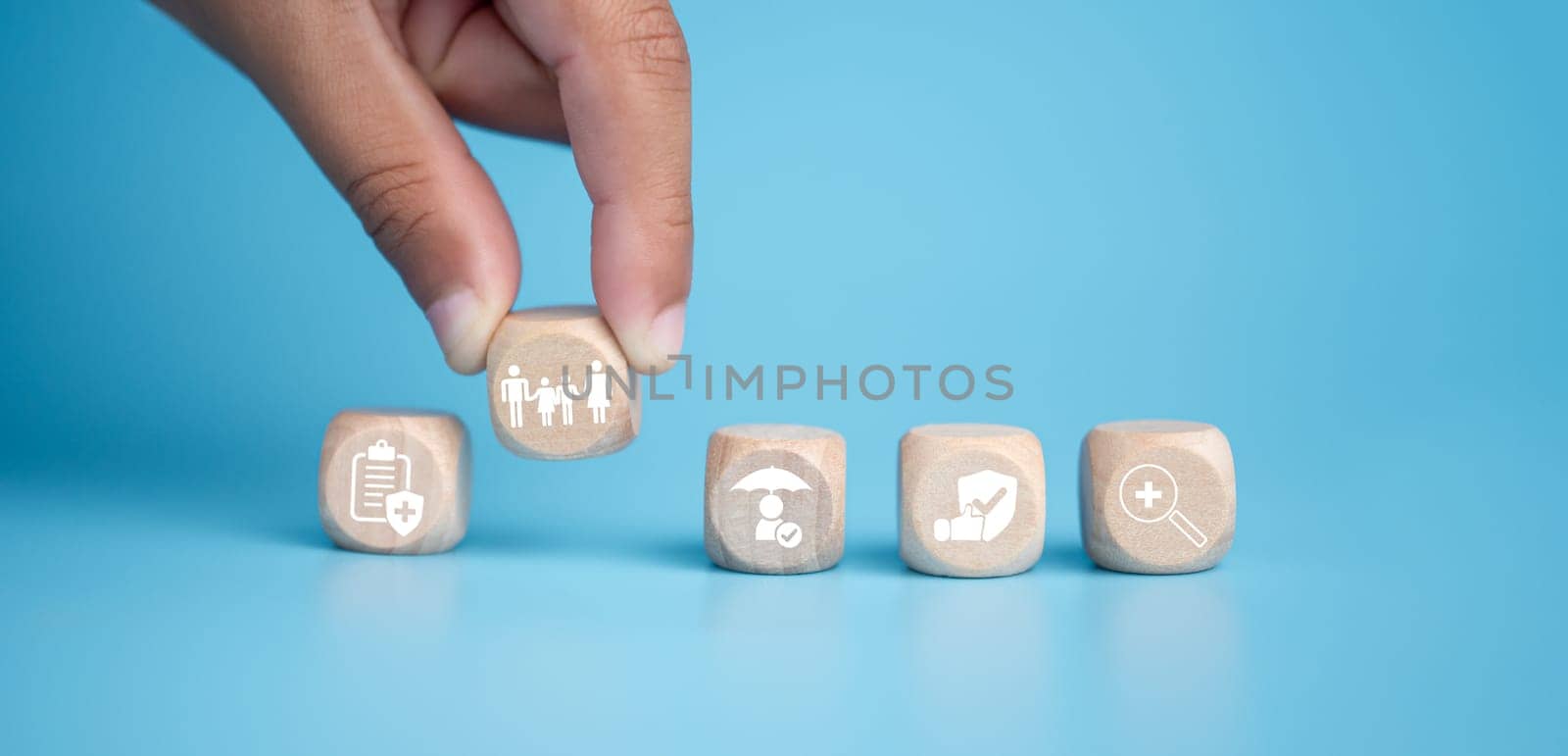 Health insurance and healthcare concept, human hand holds wooden block with icons about health insurance and healthcare access, retirement planning on blue background. by Unimages2527