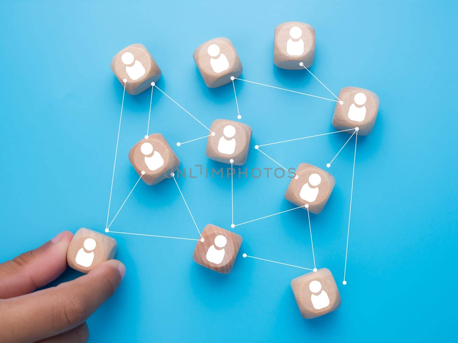 Human hand holding customer icons drawn on wooden blocks and connected together on a light blue background. Represents the selection of business goals, target customers, marketing plans and strategies, and customer-centric strategies. by Unimages2527