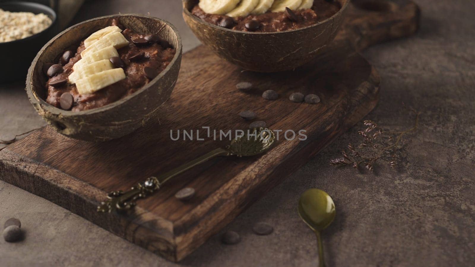 Coconut bowls with oat porridge with banana and round chocolate chips.