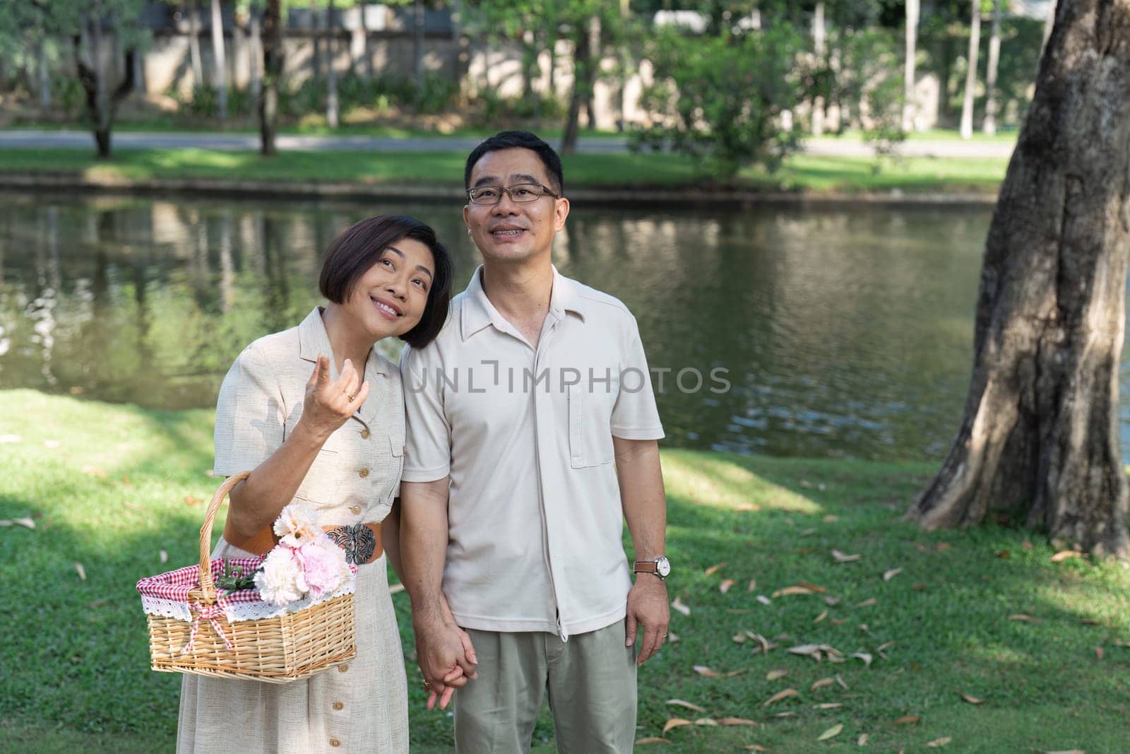 Retired couple holding hands in gardening and wife holding basket filled with flowers.