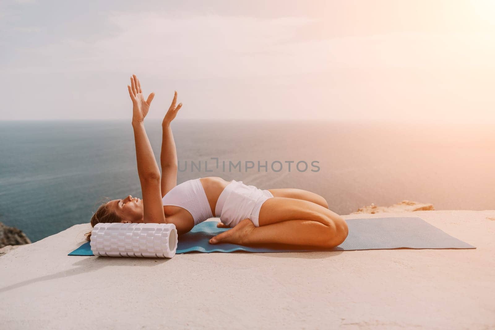 Middle aged well looking woman with black hair doing Pilates with the ring on the yoga mat near the sea on the pebble beach. Female fitness yoga concept. Healthy lifestyle, harmony and meditation.