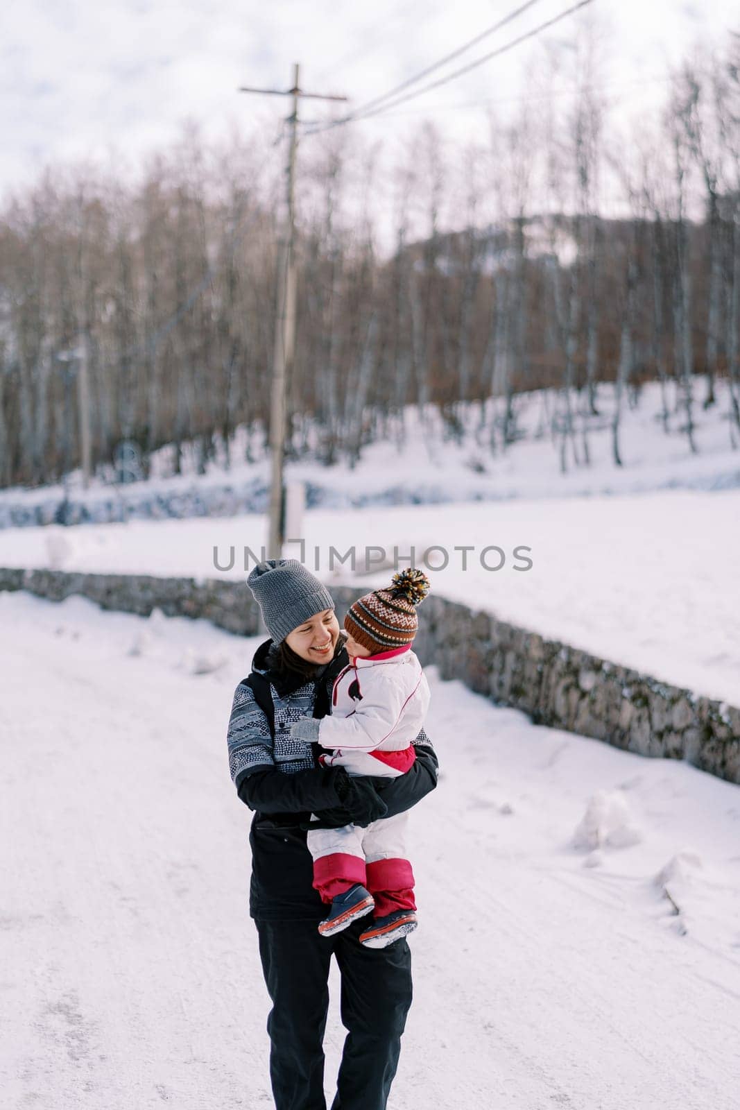 Smiling mother carries a small child on a snowy road. High quality photo