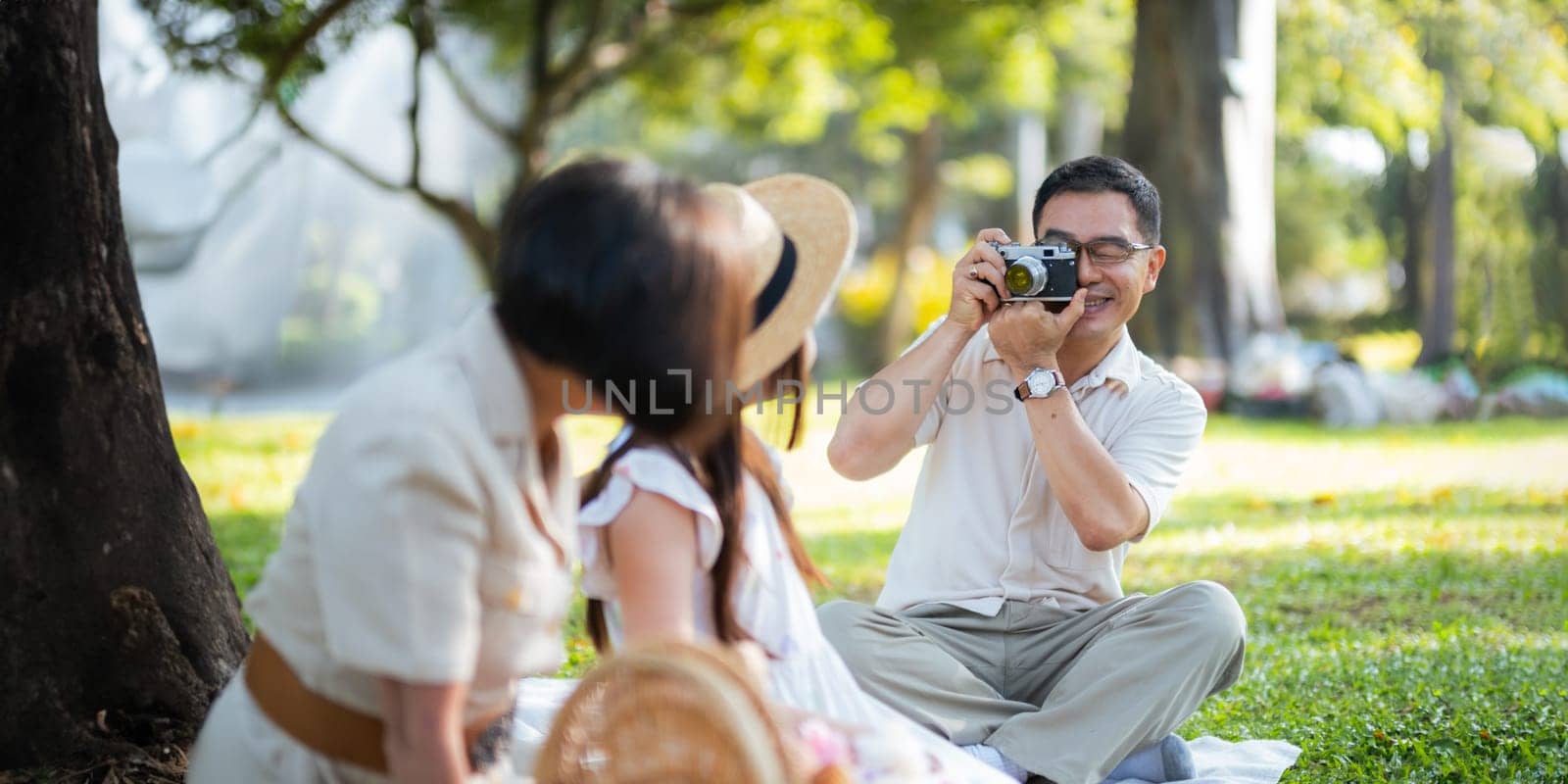 Grandpa takes pictures of granddaughter and grandma with his in park on sunny day happiness. concept grandparent and grandchild family lives together happy by nateemee