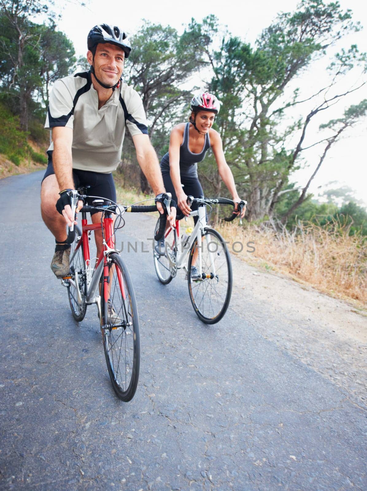 Happy couple, cycling and road in nature for, fitness, training or travel on bicycle together. Outdoor, people and exercise on bike for fun, workout and path in countryside for adventure or journey by YuriArcurs