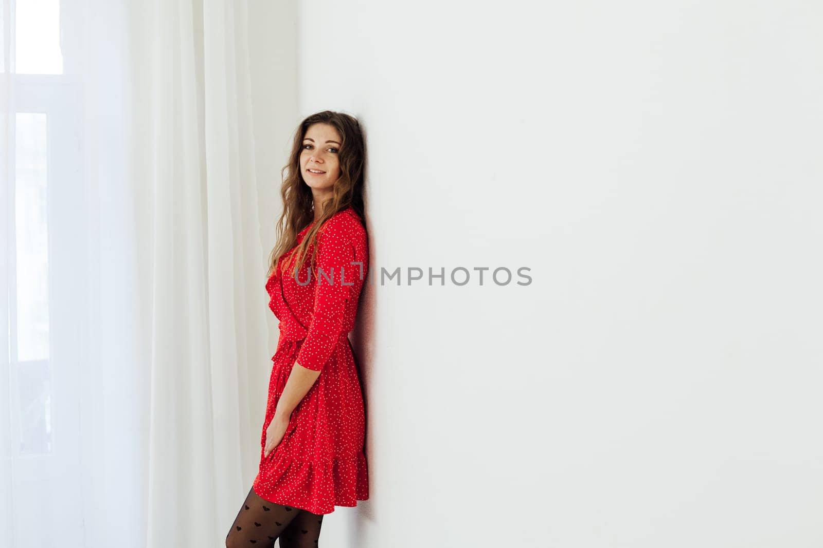 a woman in red dress stands against a white wall