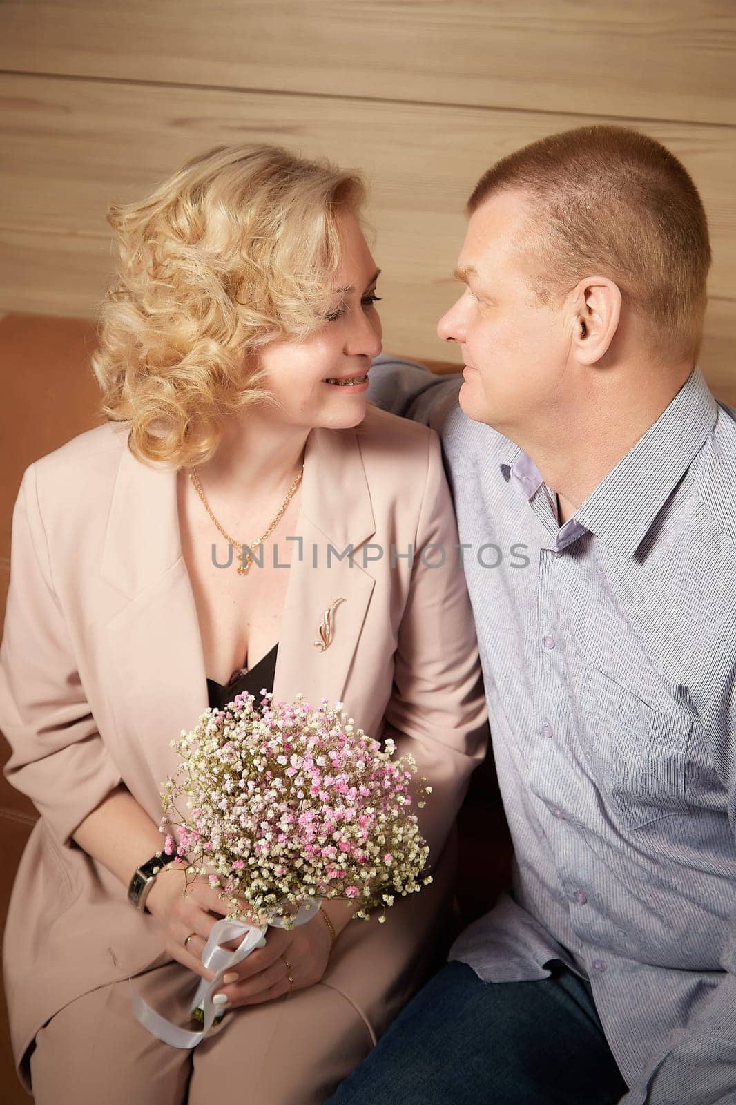 Loving adult couple communicates and embraces privately in the living room or in hotel. The woman is wearing business formal suit and man is wearing jeans and a shirt, indicating a close relationship by keleny