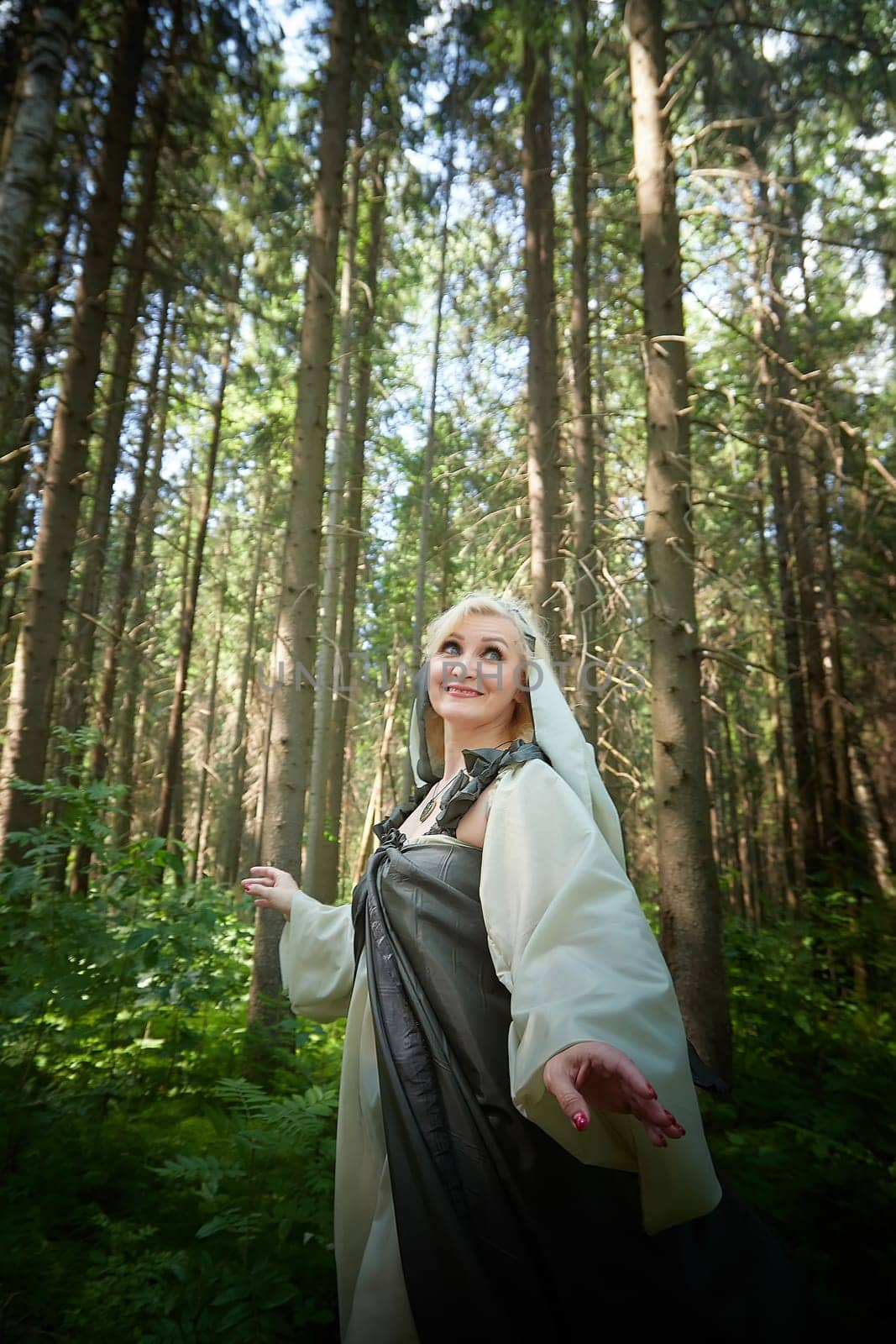 Adult mature woman 40-60 in a green long fairy dress in forest. Photo shoot in style of dryad and queen of nature. Fairy in beautiful green summer forest. Concept of caring for nature
