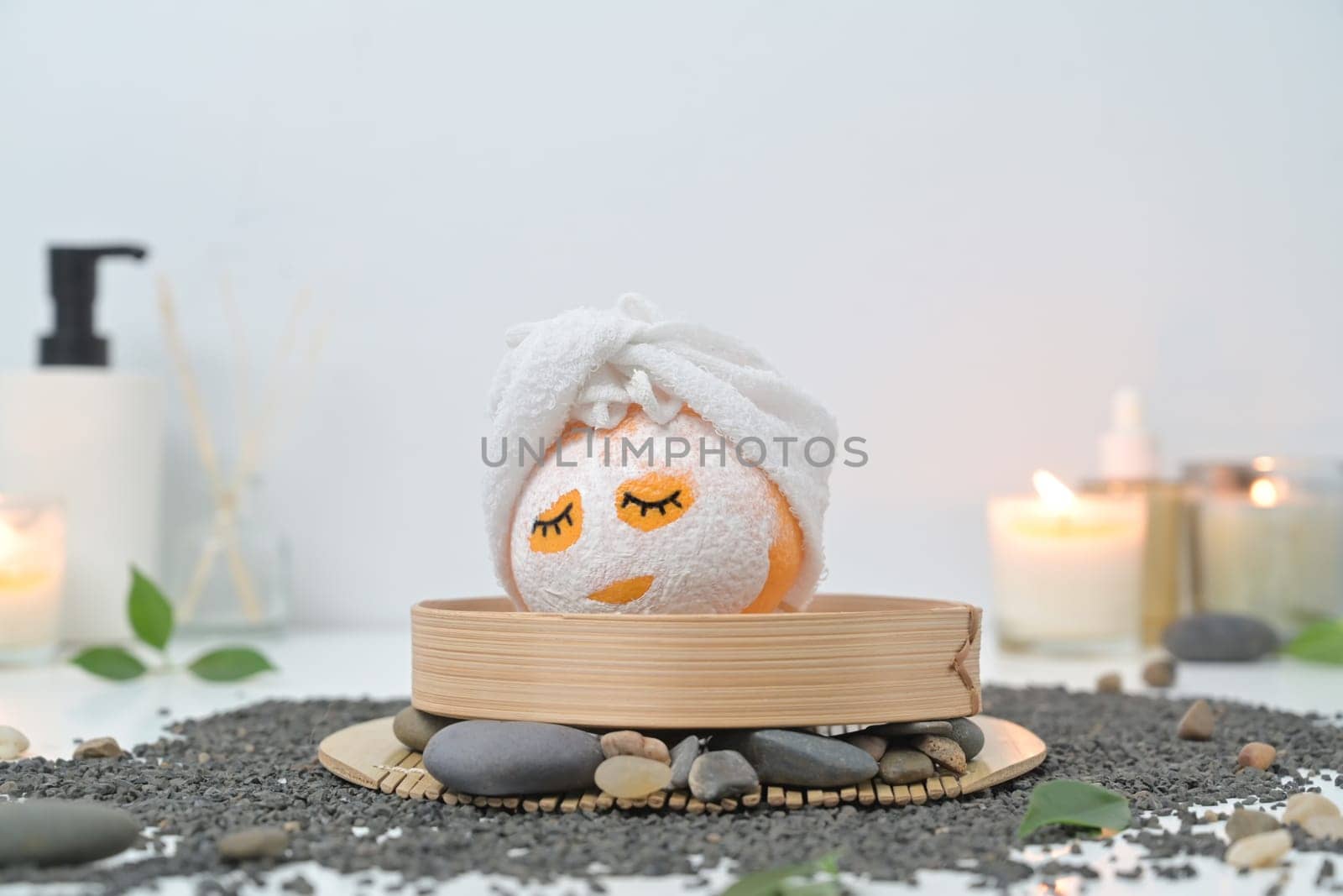 Orange fruits in face mask, zen stones, candles and green leaves on white background. Spa treatment and self care concept.