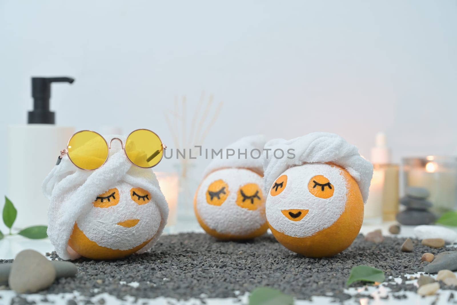 Orange fruits in face mask and towel on black pebbles. Spa treatment and self care concept.