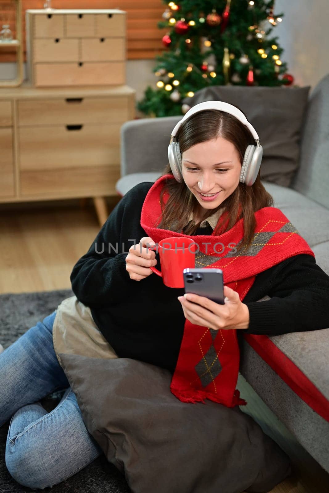 Beautiful caucasian woman drinking hot chocolate and using mobile phone in living room.