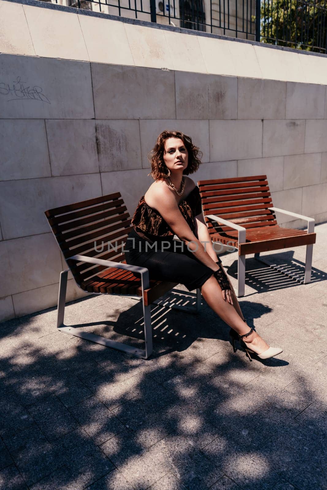 Portrait of a woman on the street. An attractive woman in a black dress is sitting on a bench outside