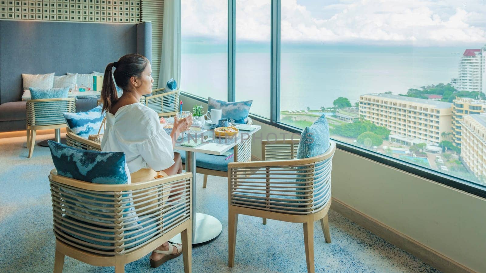 Asian Thai woman eating breakfast in a luxury hotel in Thailand, women drinking coffee looking out the window over the city and ocean