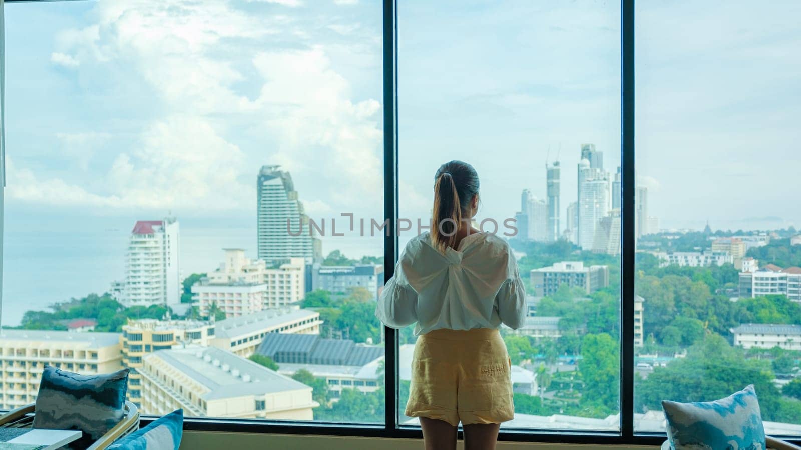 Asian Thai woman drinking coffee in the morning looking out the window of a skyscraper during breakfast in a luxury hotel in Pattaya Thailand