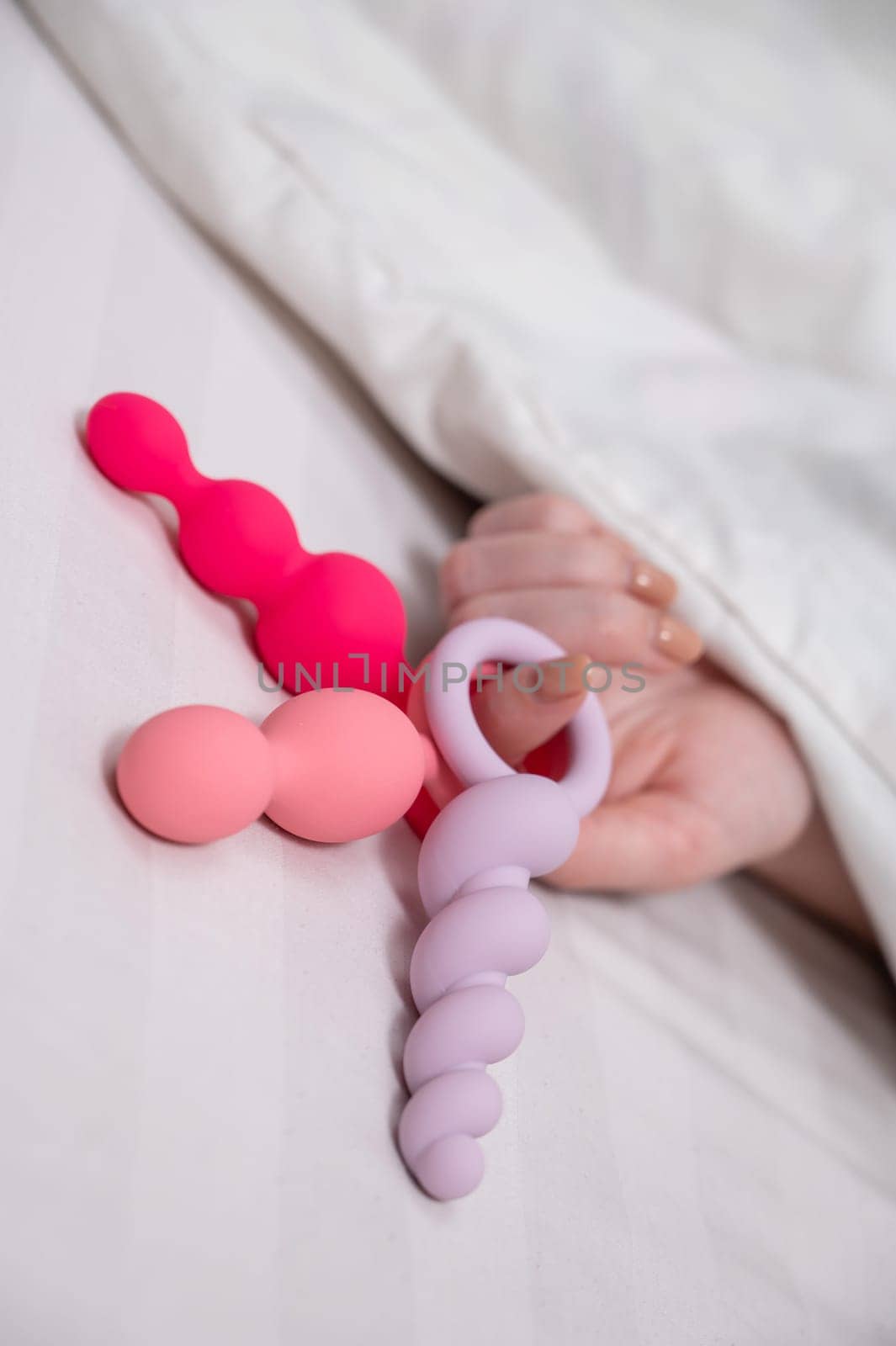 Woman holding three different anal beads while lying in bed. by mrwed54