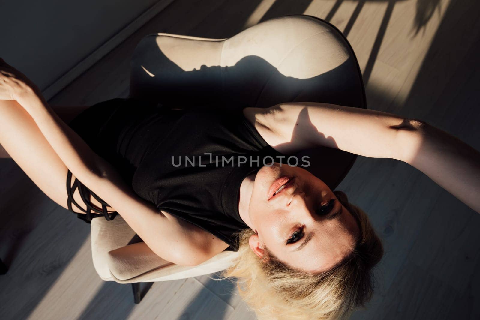 blonde woman in a black sexy dress sits in a chair in a dark room