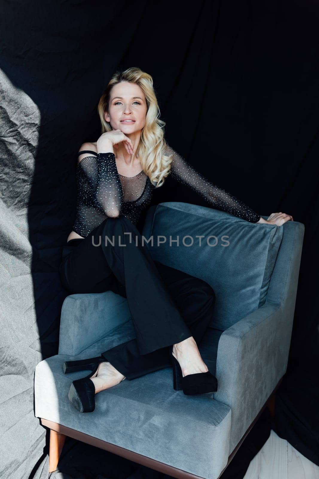 a fashionable woman in black clothes sits in a chair on a black background by Simakov