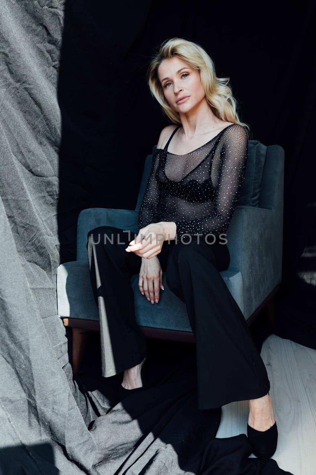 a fashionable woman in black clothes sits in a chair on a black background by Simakov