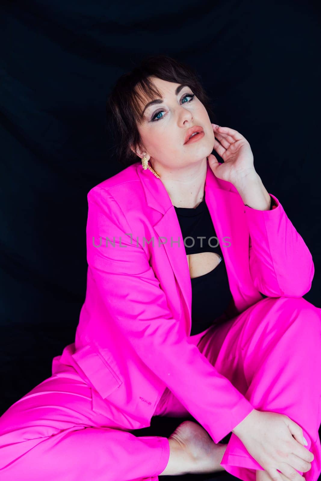 a fashionable woman in bright clothes sits on a black background by Simakov
