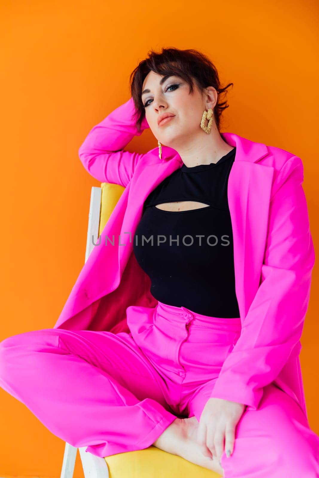 woman in bright clothes sits on a chair on an orange background