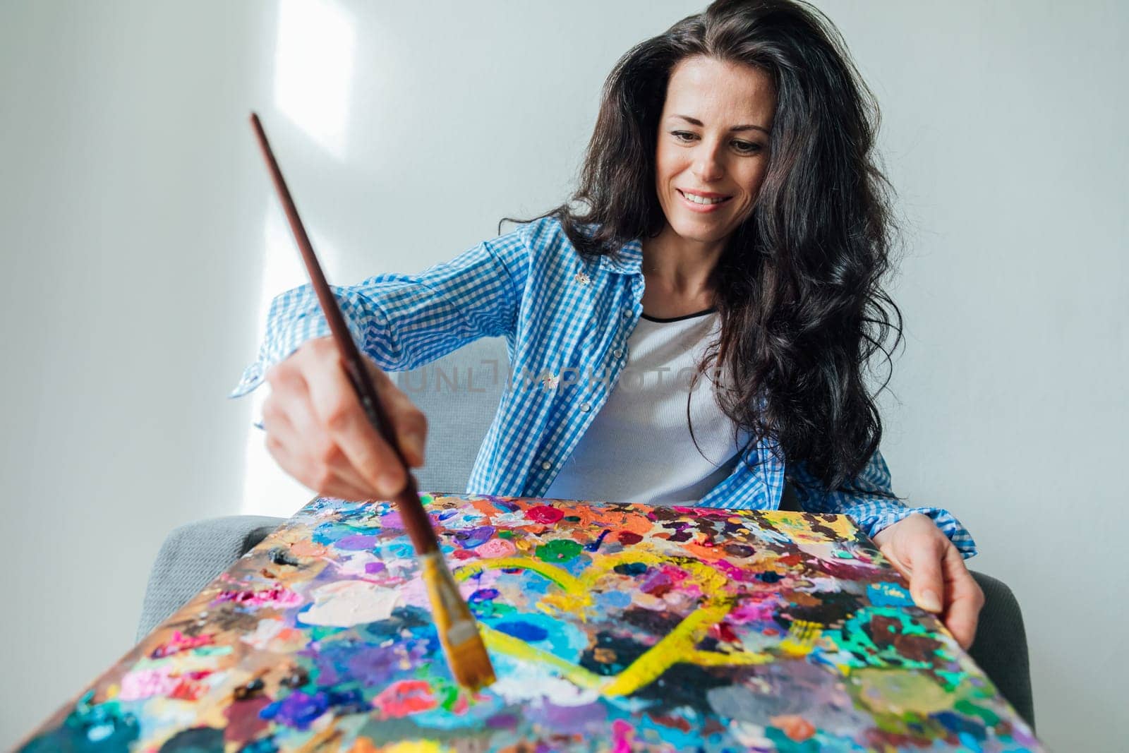 woman artist in blue clothes draws with a brush on canvas by Simakov