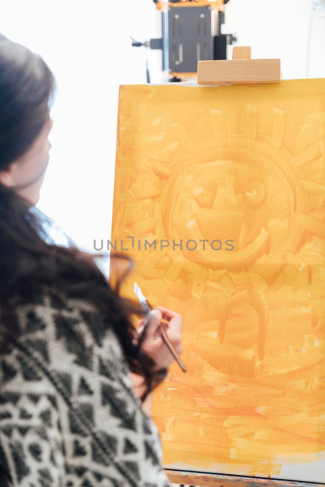 brunette woman looks at a canvas with orange paint