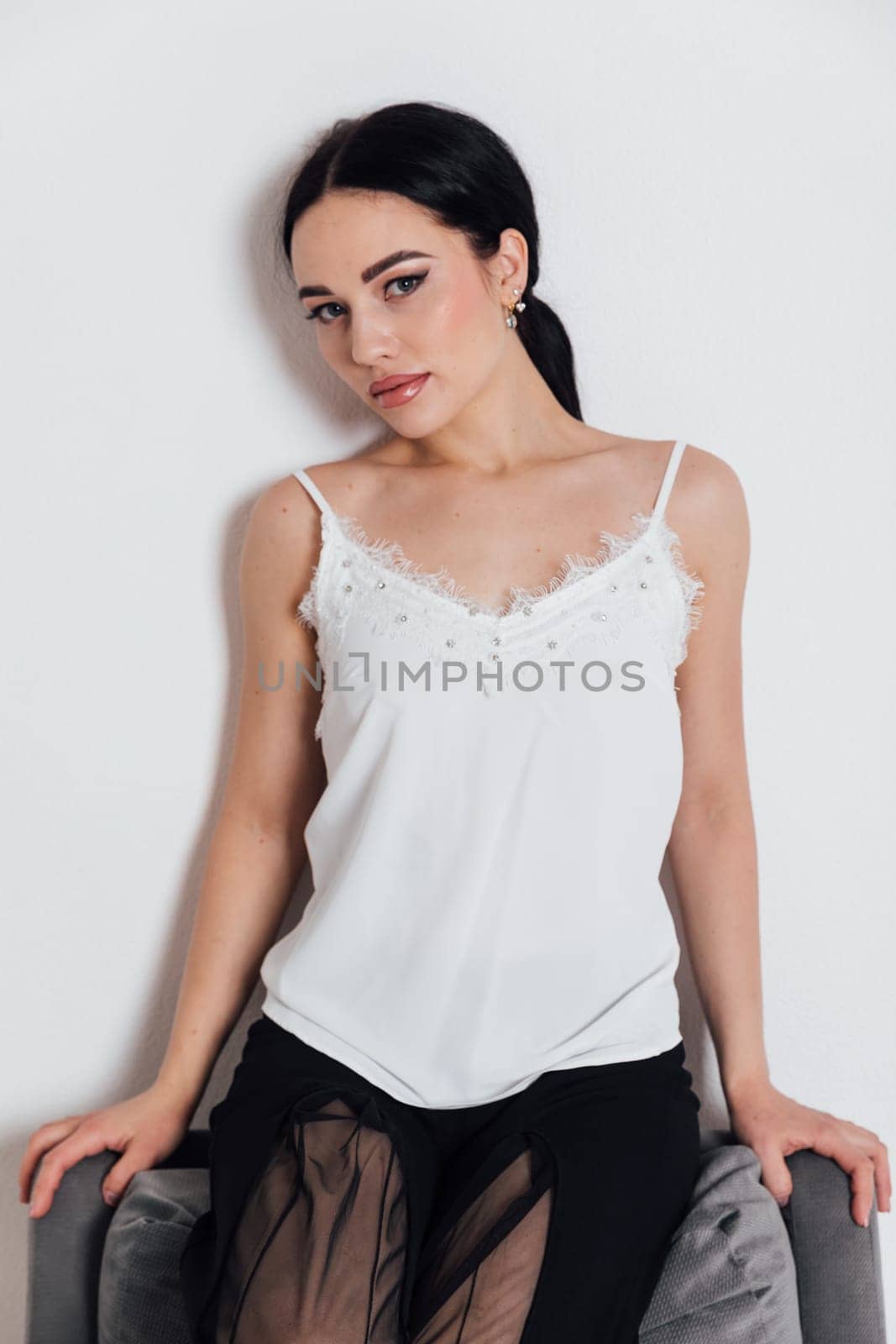 fashionable woman in a white T-shirt and black pants sits on a chair with a white background