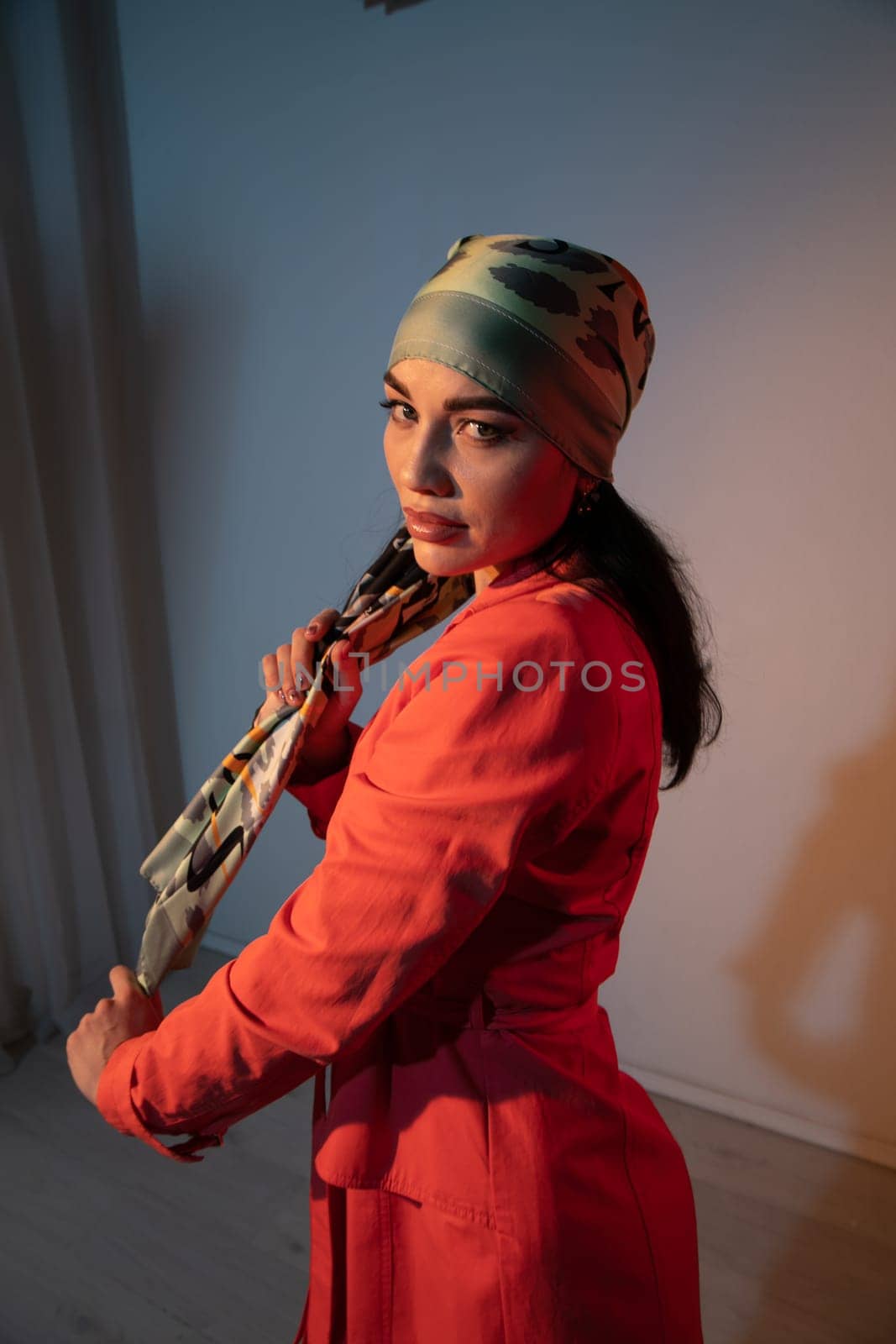 woman in a headscarf in an orange dress stands indoors