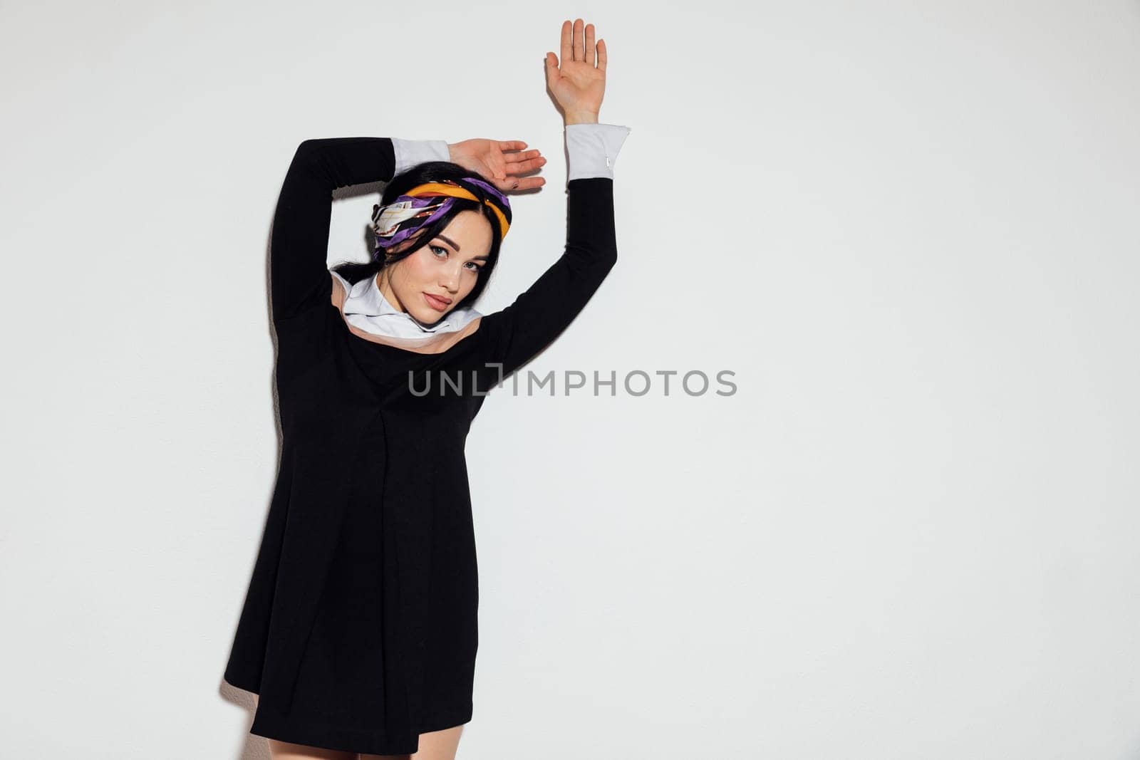 brunette woman stands on a white background with her hands raised