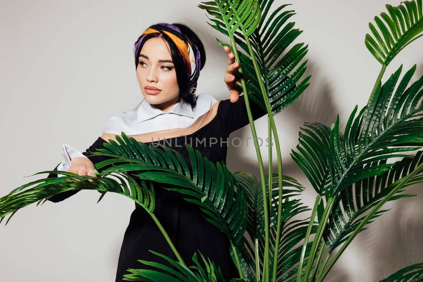 a brunette woman with a pensive look stands at a green plant by Simakov