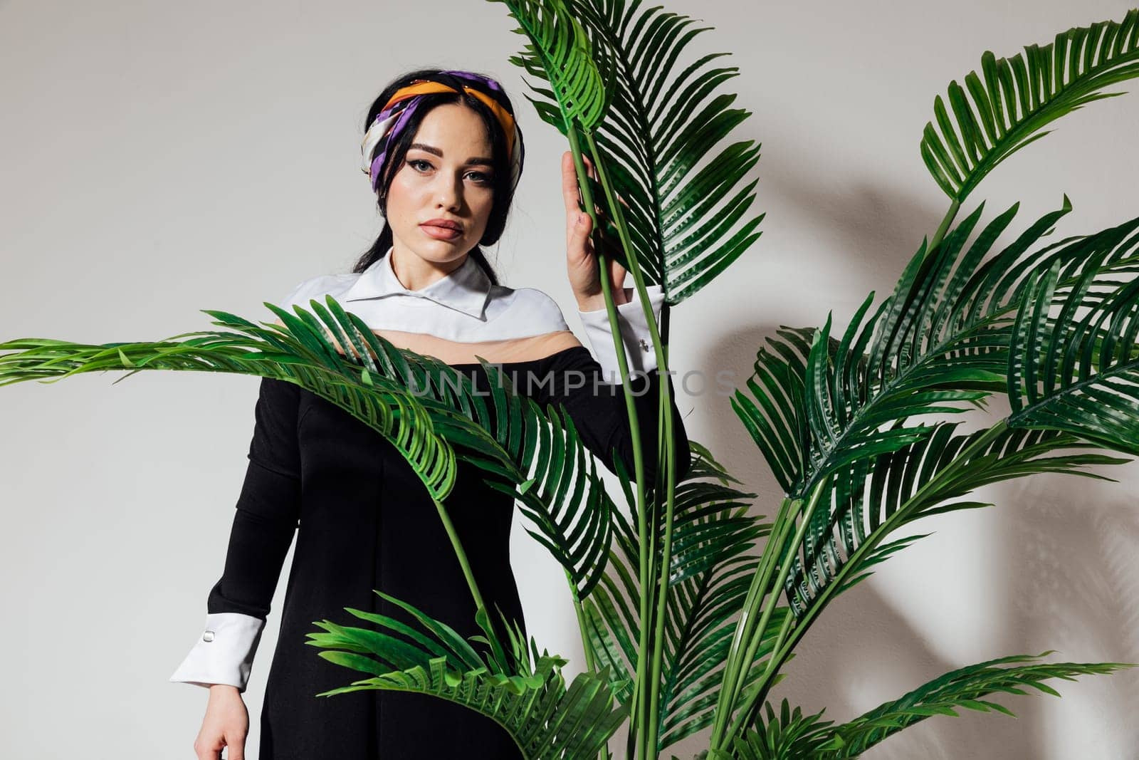 a brunette woman with a pensive look stands at a green plant by Simakov