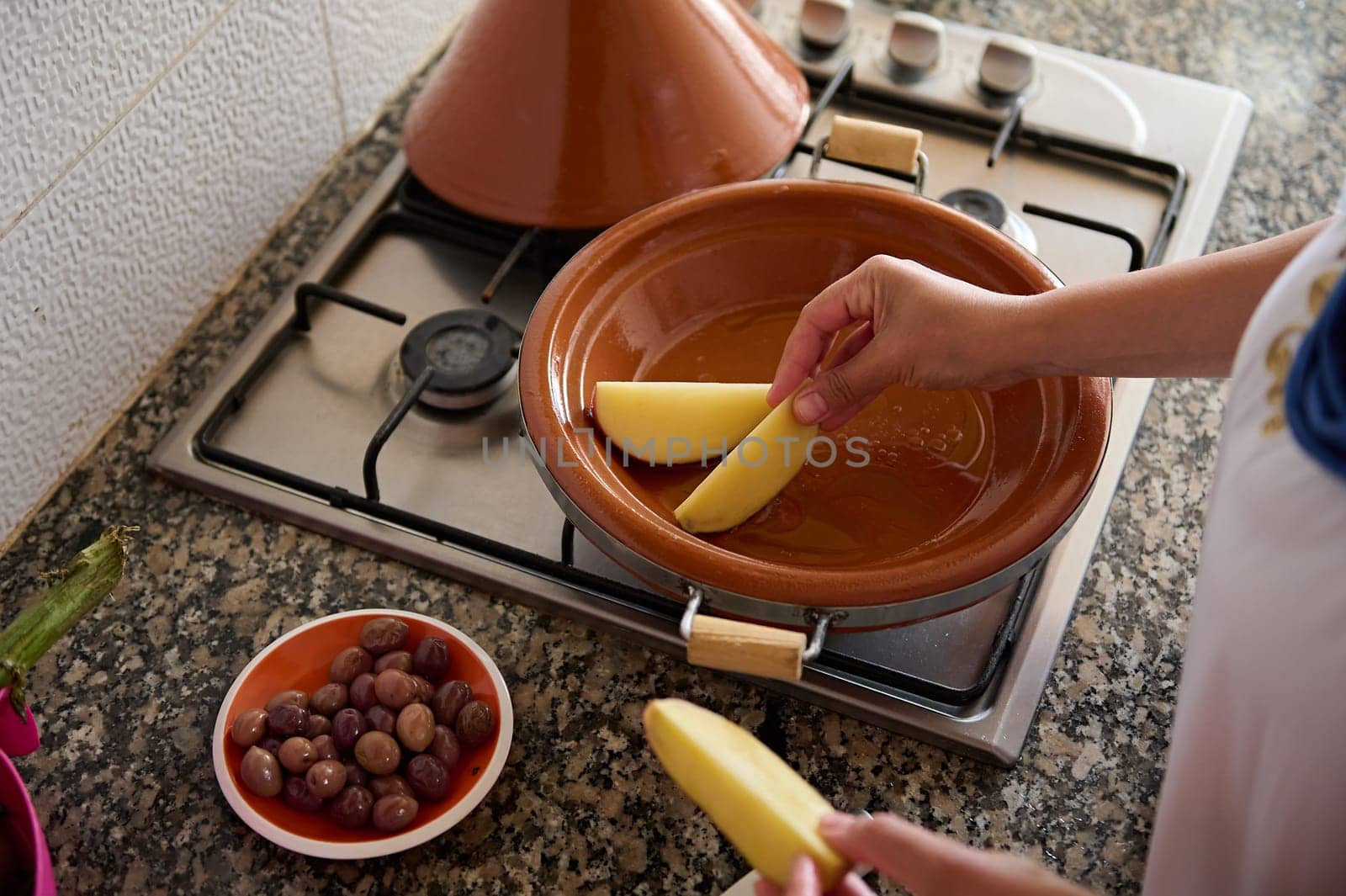 Top view of a housewife cooking tajine, putting slices of organic potato inside a clay dish. Moroccan traditional food by artgf