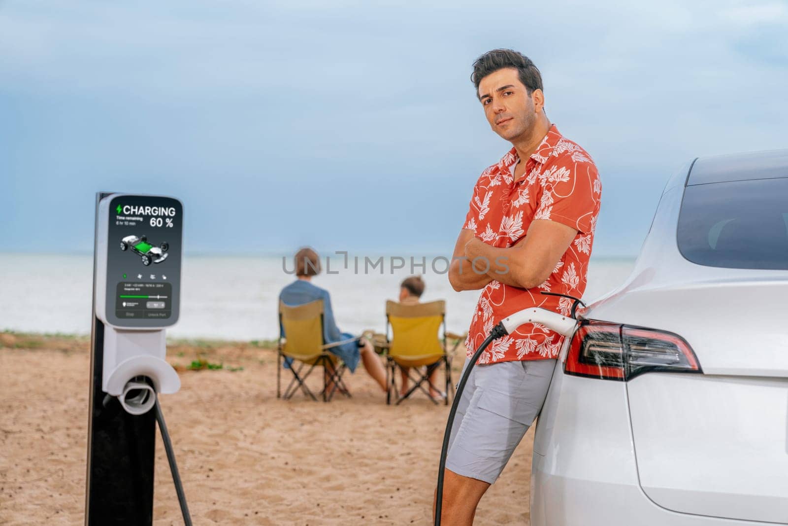 Family vacation trip traveling by the beach with electric car, dad or father recharge EV car while his family enjoy seascape beach. Family trip with alternative energy and eco-friendly car. Perpetual