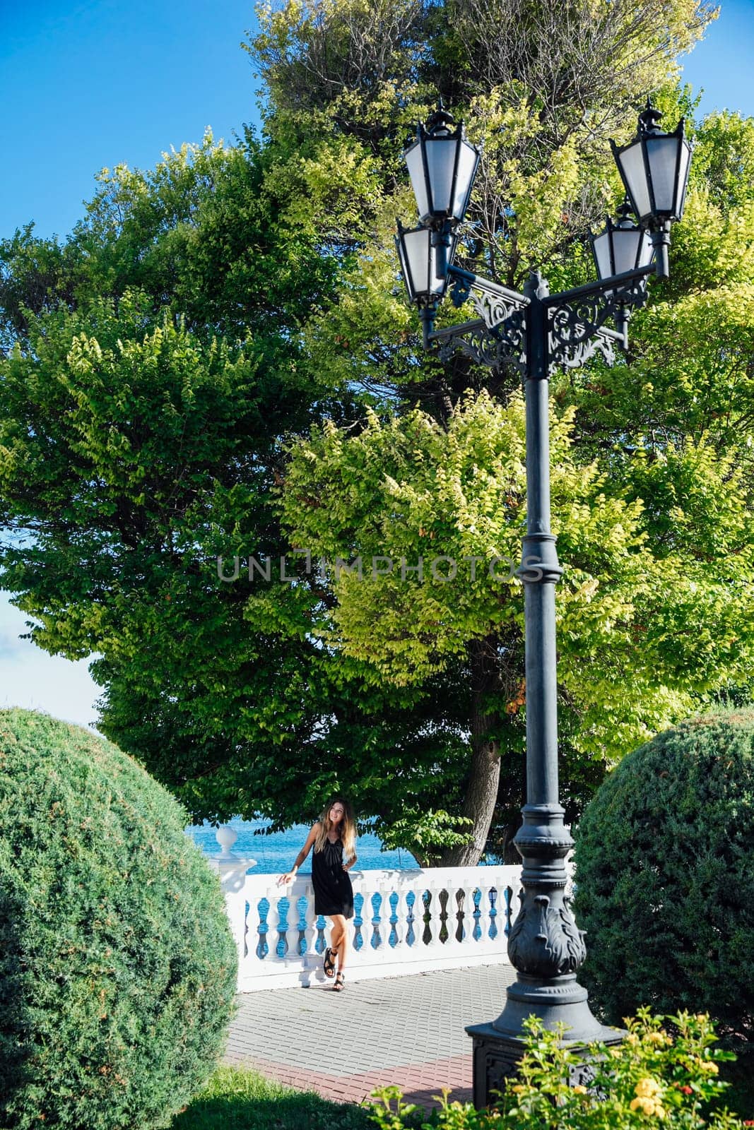 a woman in a black dress and stands by the railing near the sea in the park walk