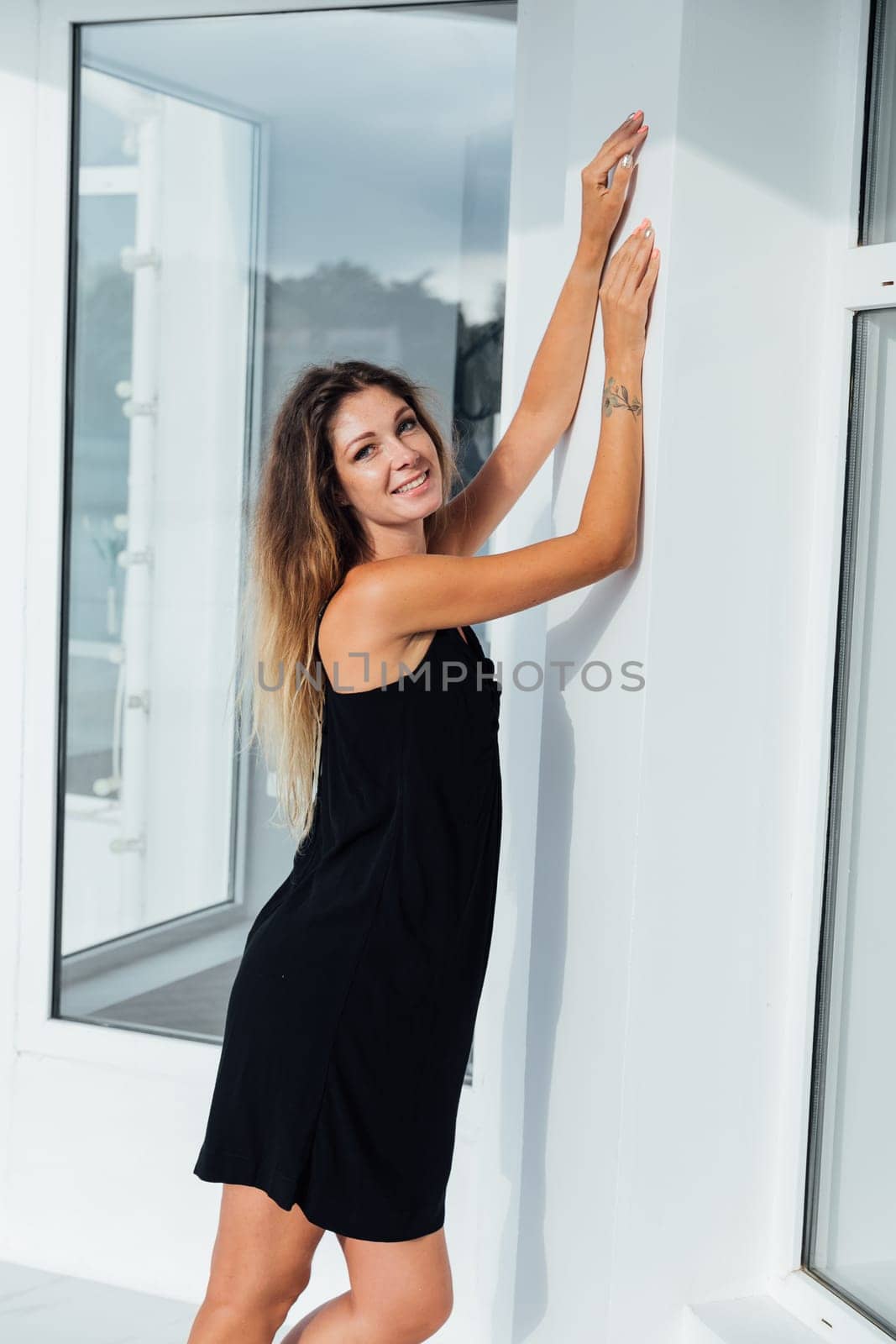 a woman stands against a white wall with her hands on top of the windows by Simakov