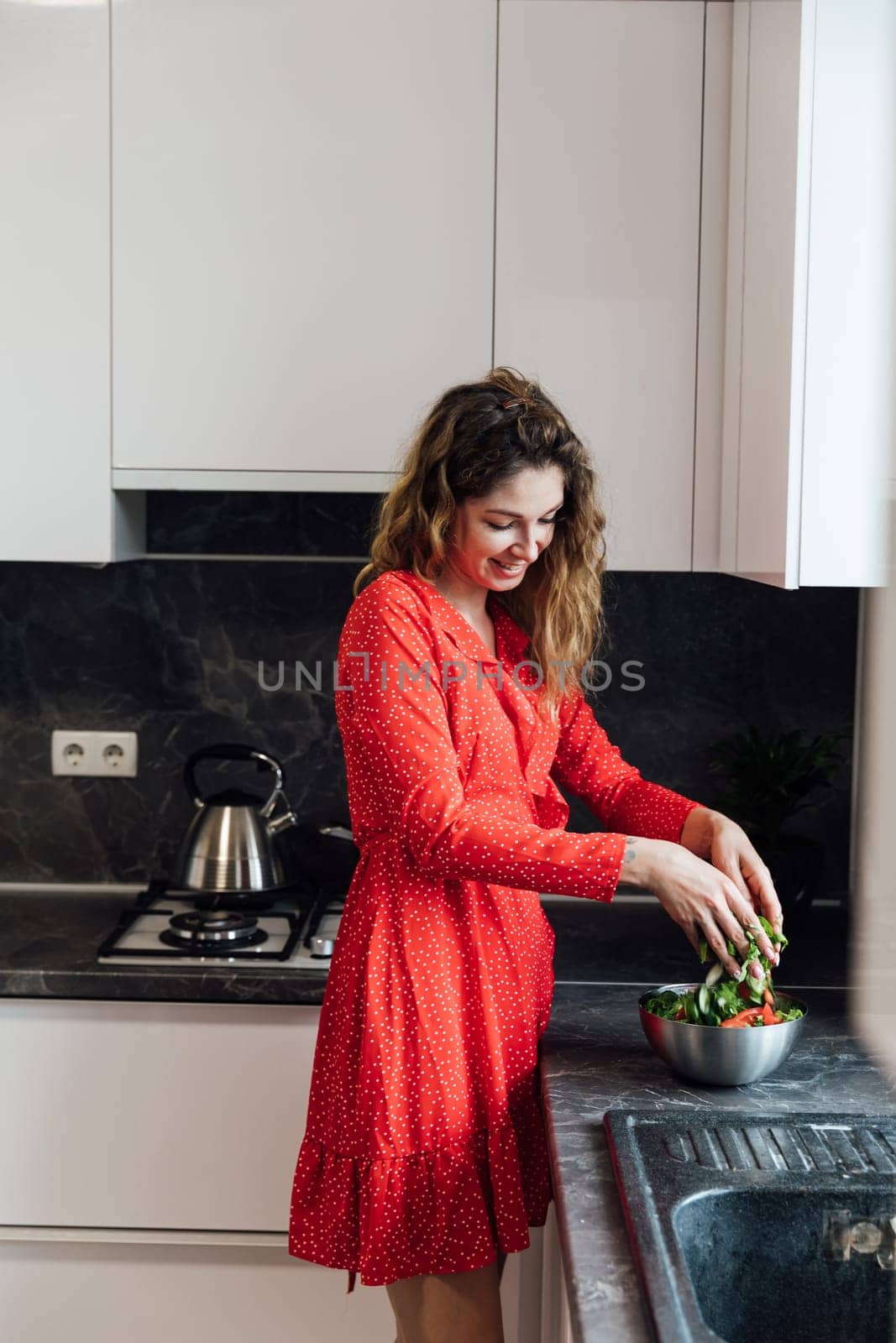 woman in a red dress prepares a salad in the kitchen