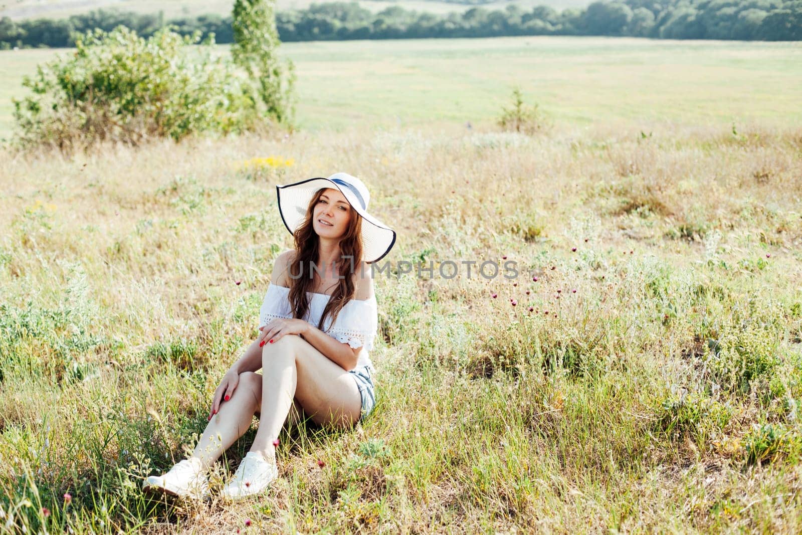 beautiful woman in a hat sits on dry grass in a field