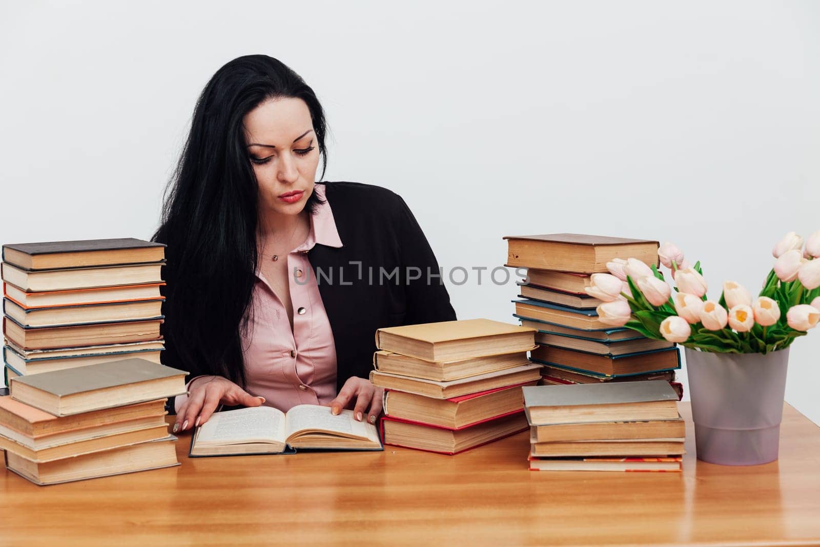 woman in the library sits and reads a book at a table near a stack of books
