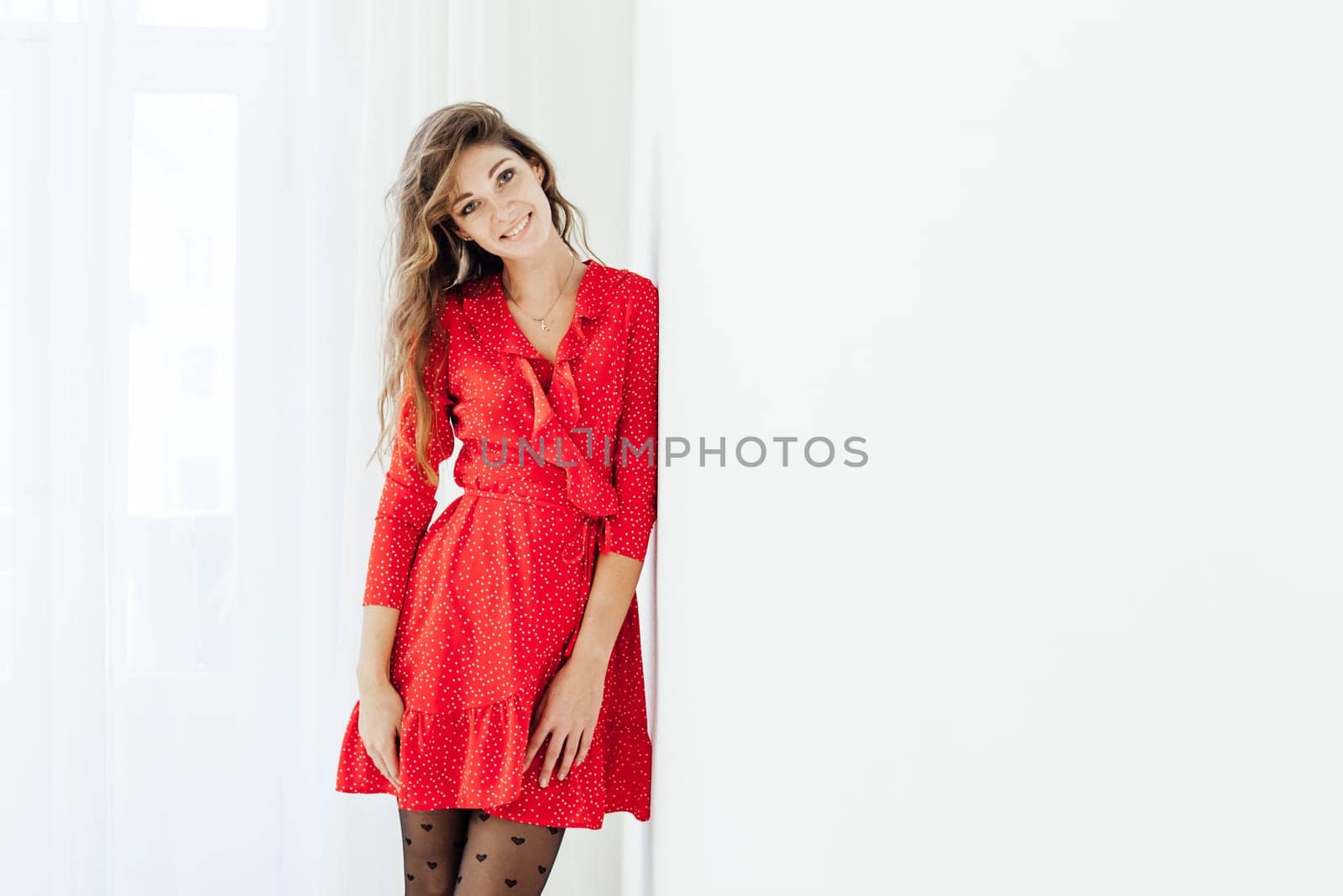 beautiful woman in a red dress stands against a white wall posing
