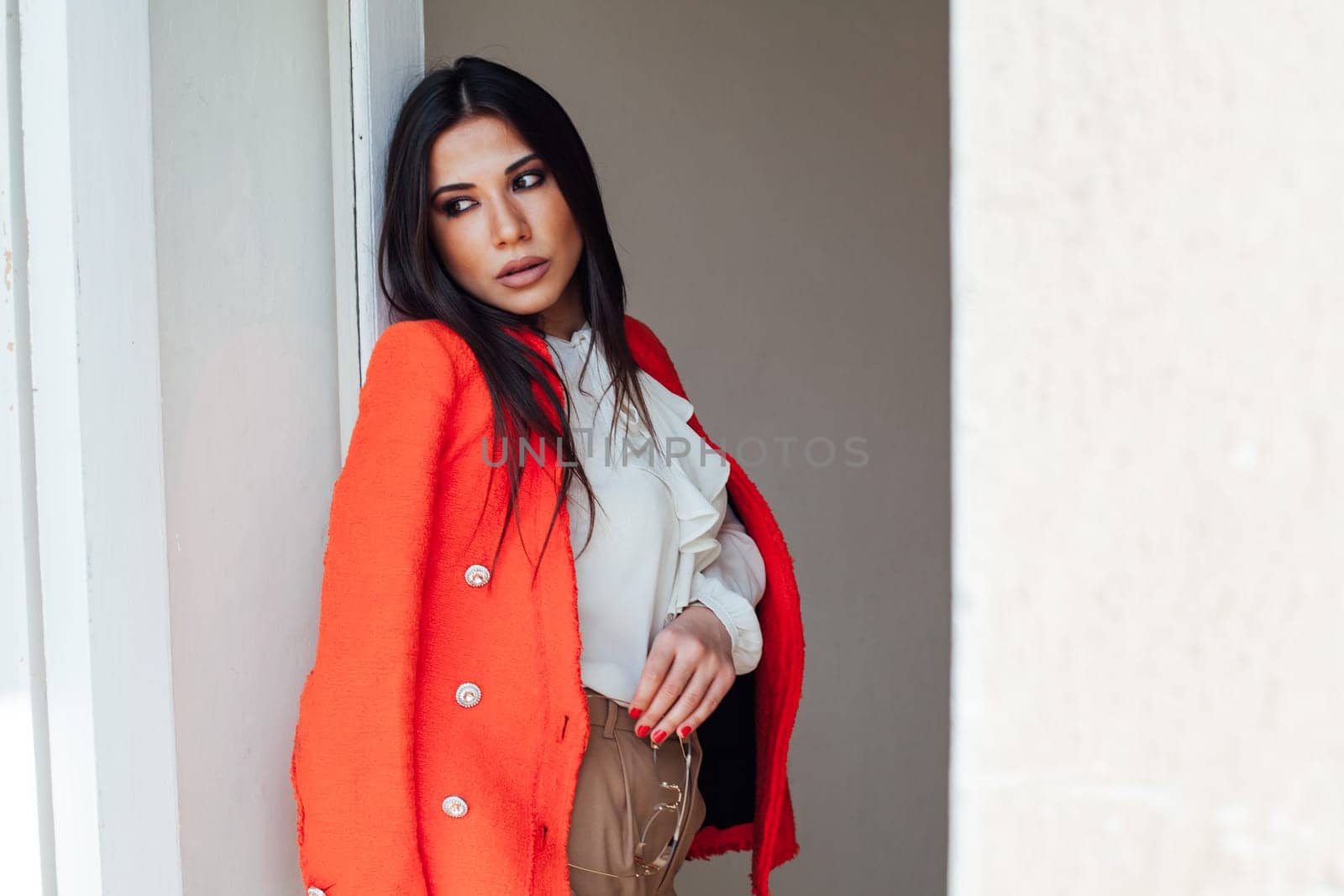 a woman fashionable brunette in a bright jacket business style in the office stands against the wall