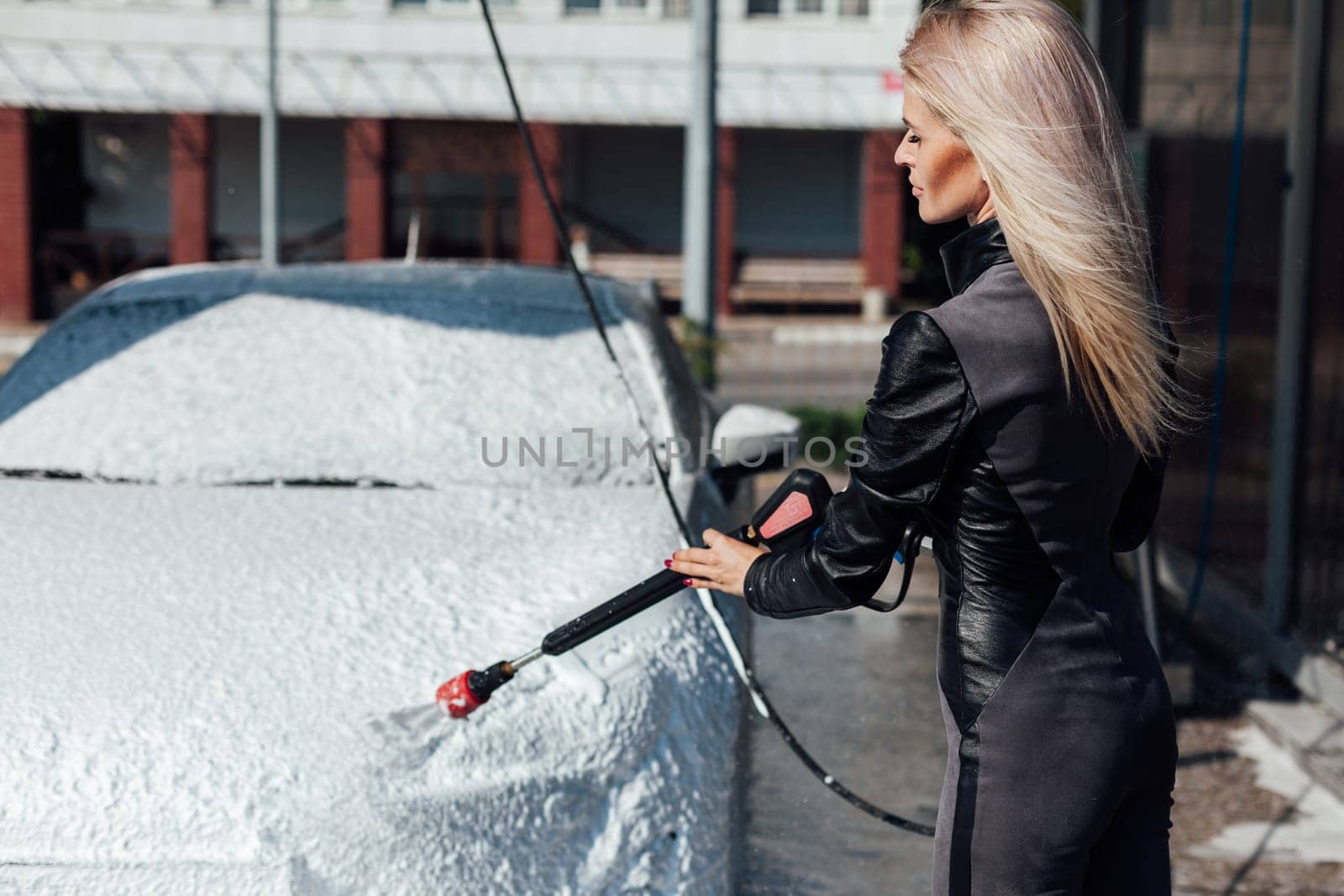 blonde woman washes a car at a car wash clean car water in a hose for a car