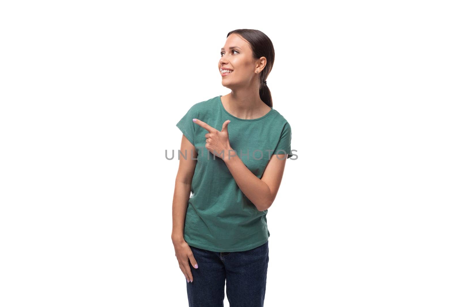 a young smiling woman with black hair and a slim figure dressed in a green T-shirt points with her hand and an empty white space for advertising.