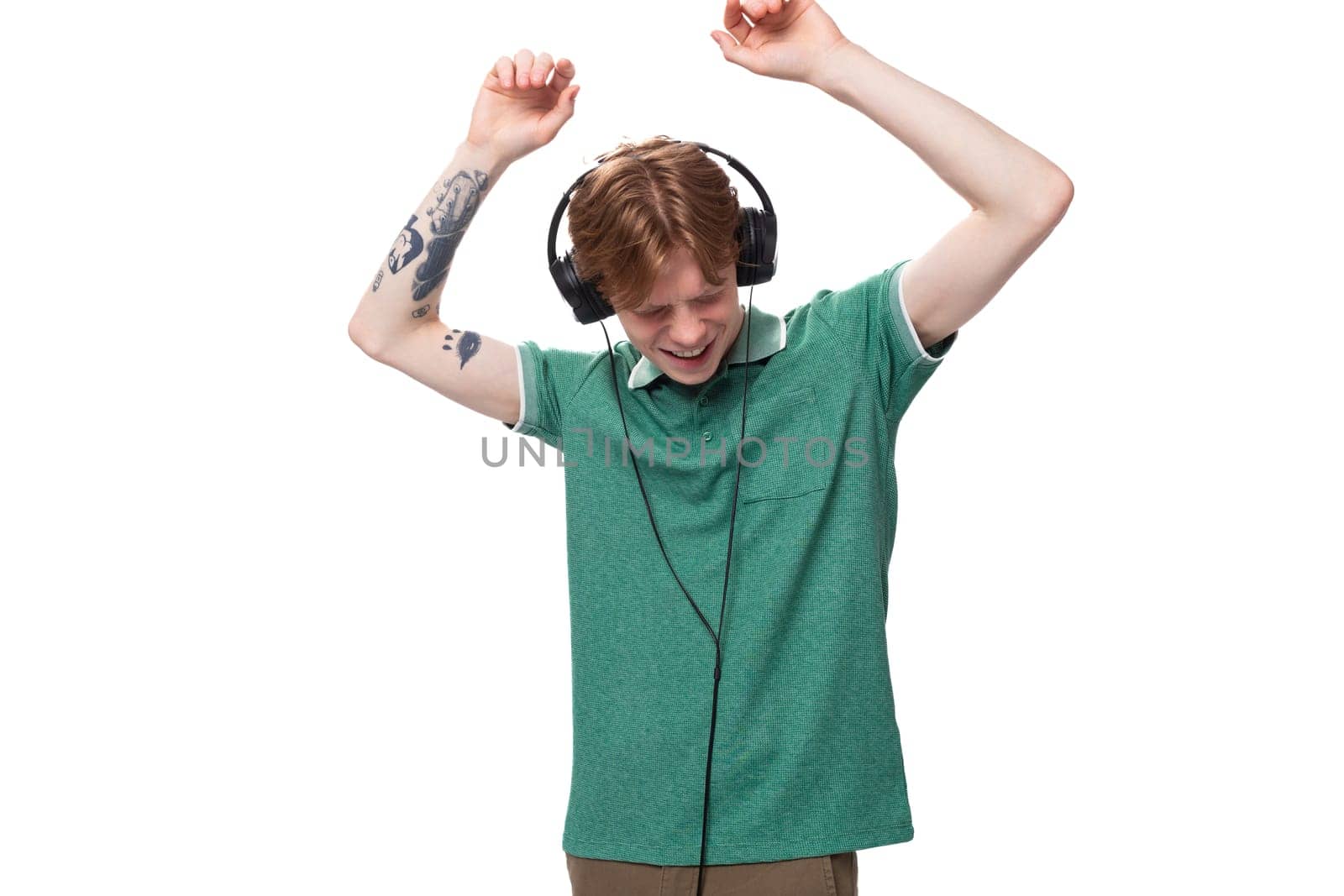 a young man with red hair dressed in a green t-shirt in wireless large headphones dances and enjoys.