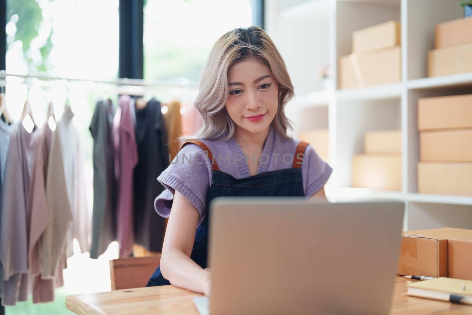 Starting small business entrepreneur of independent young Asian woman online seller is using computer and taking orders to pack products for delivery to customers. SME delivery concept by Manastrong