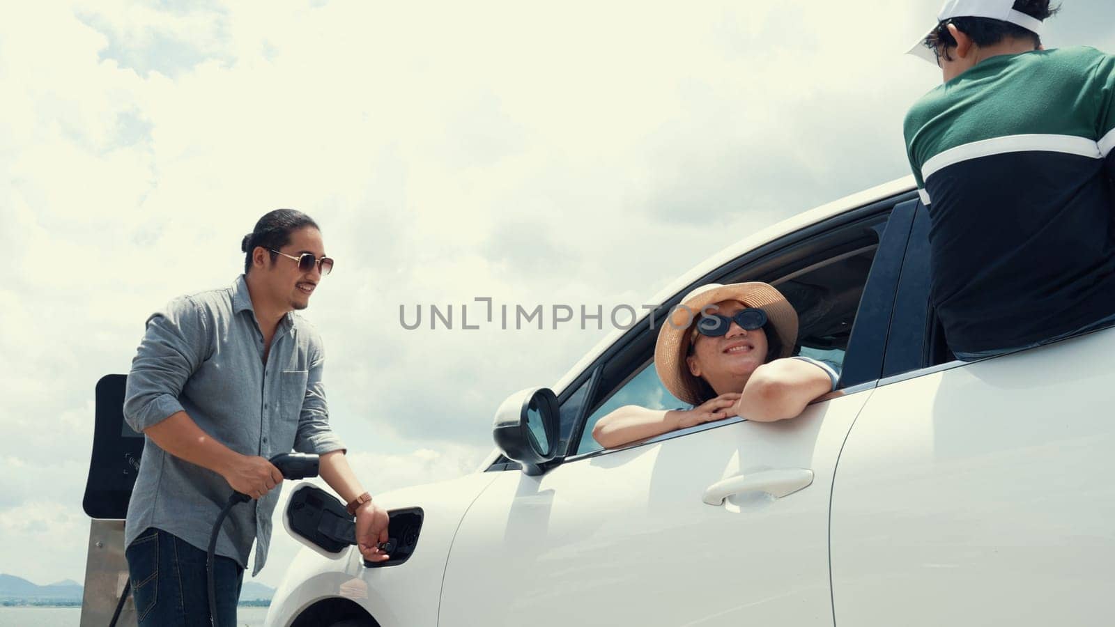 Concept of progressive happy family enjoying their time at wind farm with electric vehicle. Electric vehicle driven by clean renewable energy from wind turbine generator for charging station.