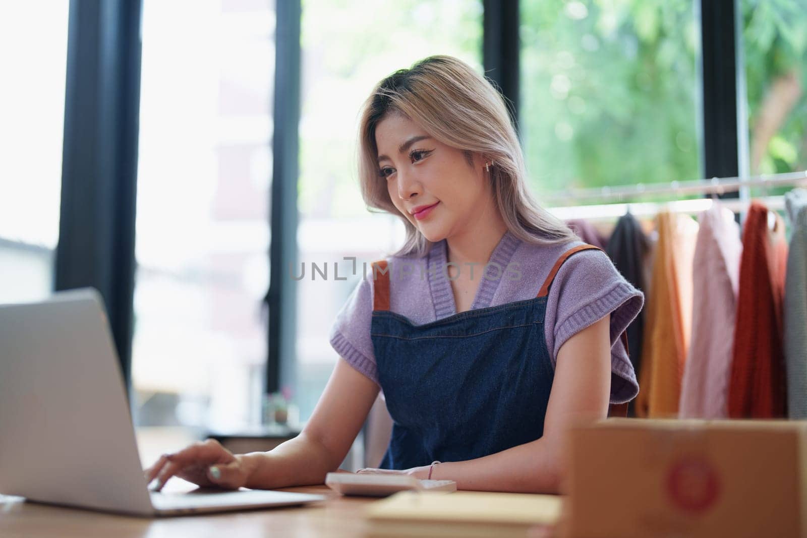 Starting small business entrepreneur of independent young Asian woman online seller is using computer and taking orders to pack products for delivery to customers. SME delivery concept by Manastrong