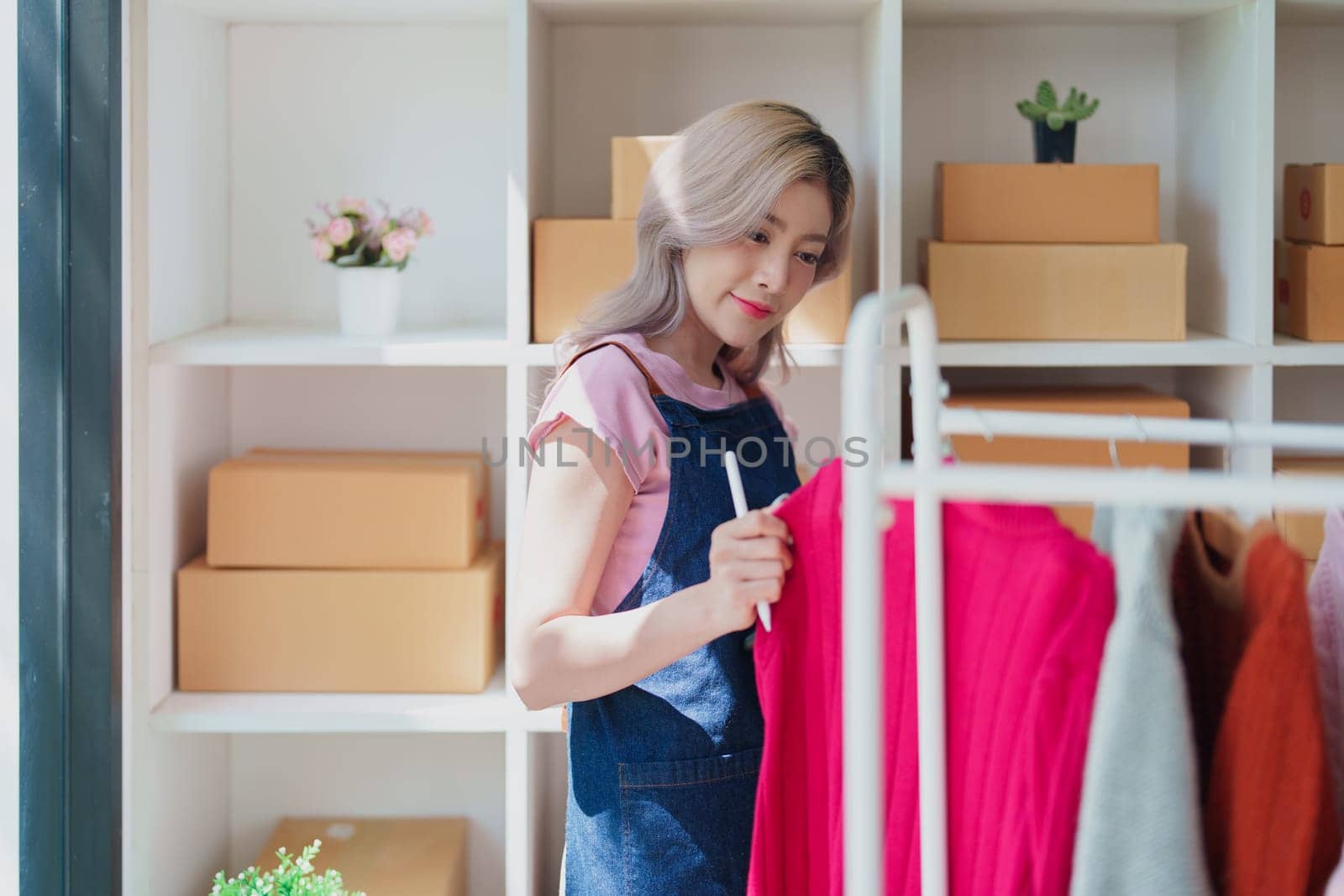 Portrait Of Asian Female Owner Of Fashion Store Checking Stock In Clothing Store With using notebook successful happy smile at small business, sme or ecommerce concepts.