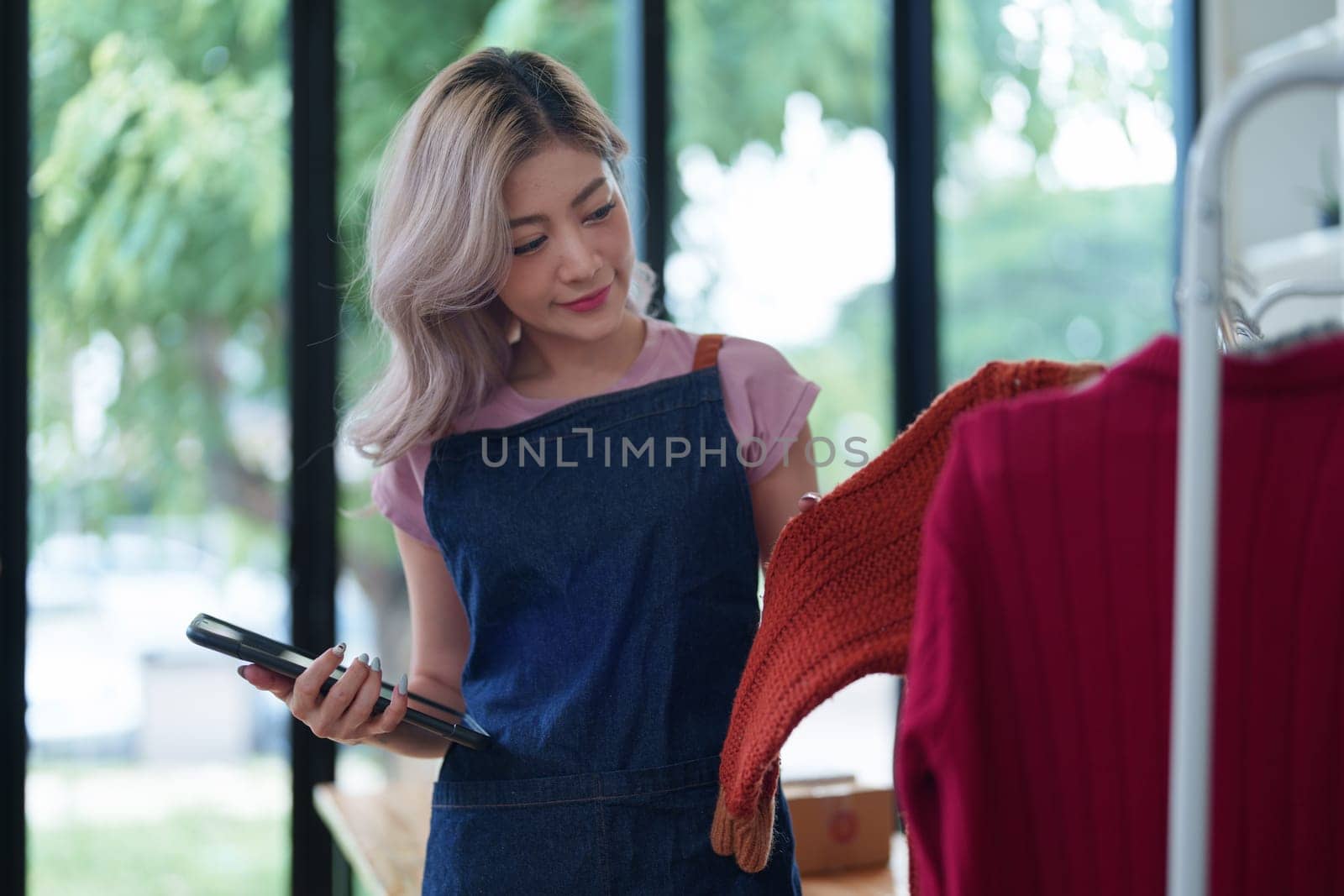 Portrait Of Asian Female Owner Of Fashion Store Checking Stock In Clothing Store With using notebook successful happy smile at small business, sme or ecommerce concepts by Manastrong