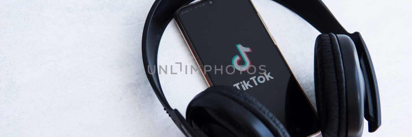 Tver, Russia-August 5, 2020, the tik tok logo on the smartphone screen on a light background with large headphones. Tik-Tok icon. logo of the current app. Tiktok social network. by Annu1tochka